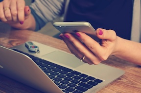 Hands using a phone beside a computer